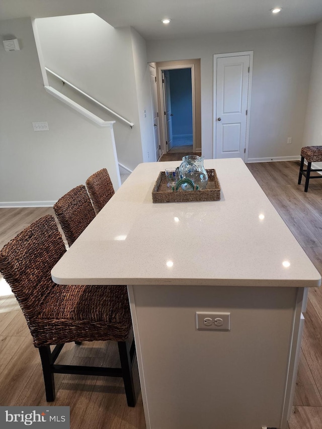 kitchen with baseboards, a kitchen island, wood finished floors, light countertops, and recessed lighting