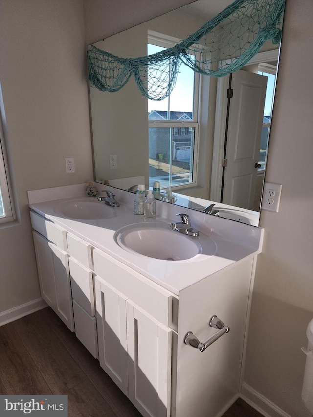 bathroom featuring double vanity, wood finished floors, a sink, and baseboards