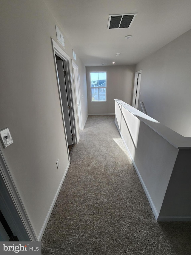 hallway with baseboards, visible vents, and light colored carpet