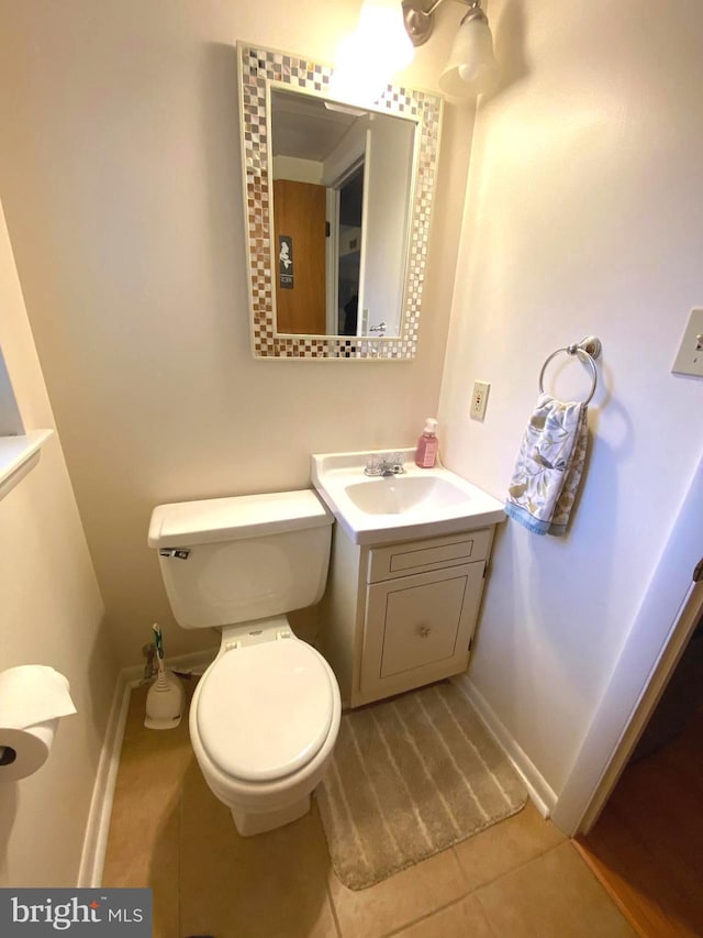 half bathroom featuring tile patterned flooring, toilet, vanity, and baseboards