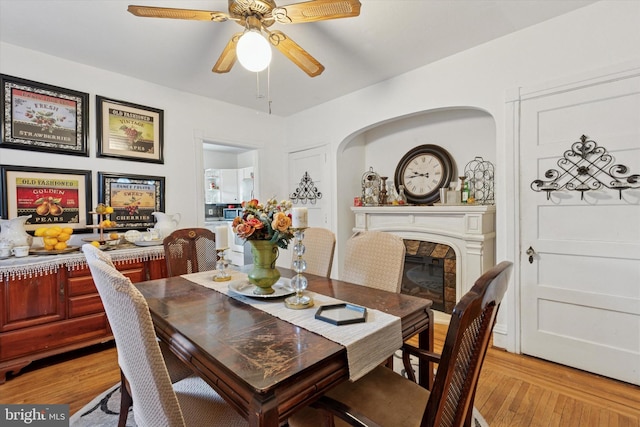 dining room featuring a glass covered fireplace, light wood-style floors, arched walkways, and ceiling fan