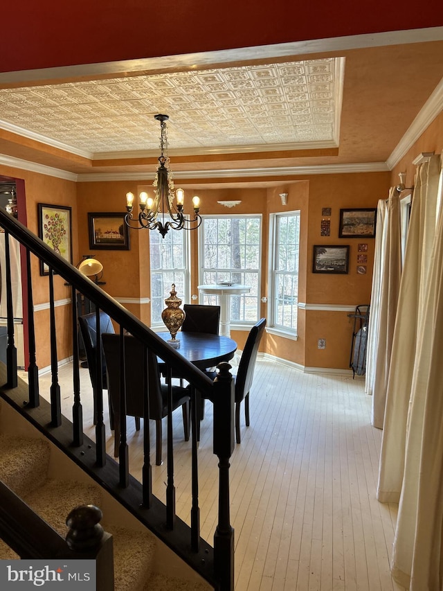 dining area featuring stairs, a tray ceiling, wood-type flooring, an ornate ceiling, and crown molding