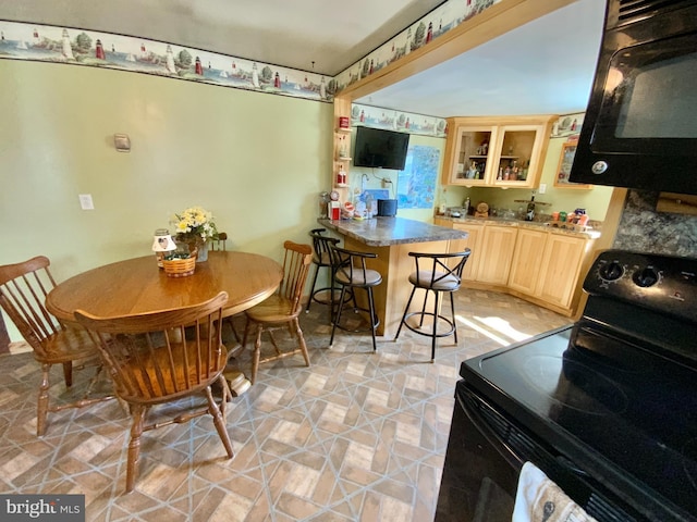 kitchen with glass insert cabinets, a kitchen breakfast bar, a peninsula, light brown cabinetry, and black appliances