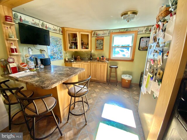 kitchen featuring glass insert cabinets, light brown cabinets, a kitchen breakfast bar, a peninsula, and baseboards