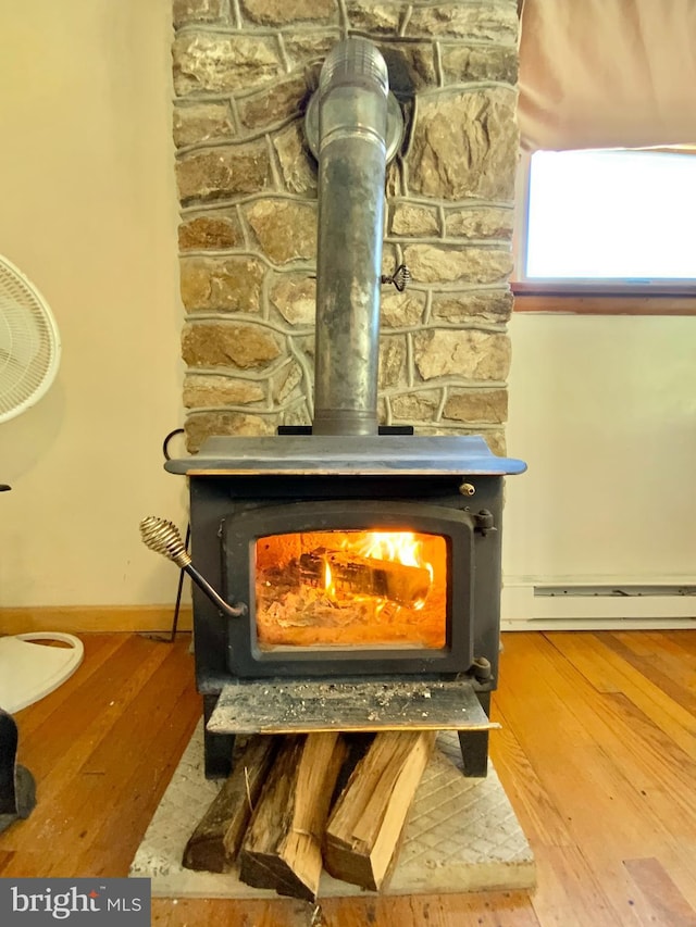 details with a baseboard heating unit, wood finished floors, a wood stove, and baseboards