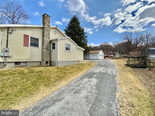 view of side of home with a garage, a chimney, an outdoor structure, and a lawn