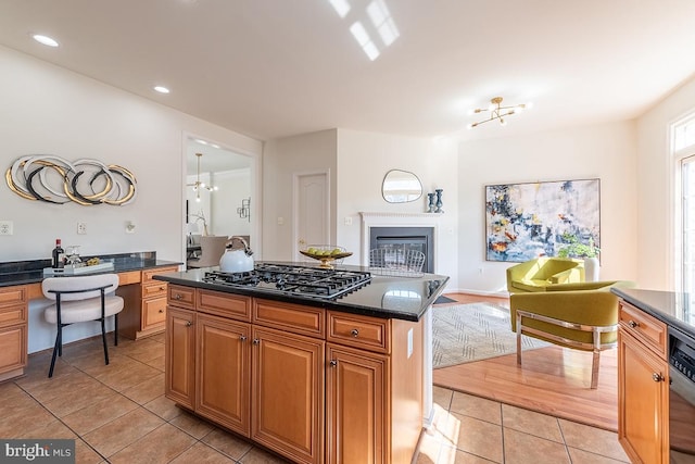 kitchen featuring light tile patterned floors, black gas stovetop, open floor plan, built in desk, and a glass covered fireplace