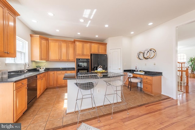 kitchen featuring a breakfast bar, dark countertops, built in study area, a kitchen island, and black appliances