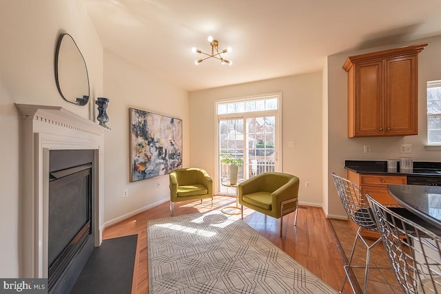 living area with an inviting chandelier, baseboards, wood finished floors, and a glass covered fireplace