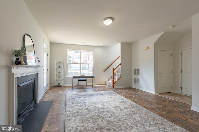 unfurnished living room with stone finish floor, stairs, baseboards, and a glass covered fireplace