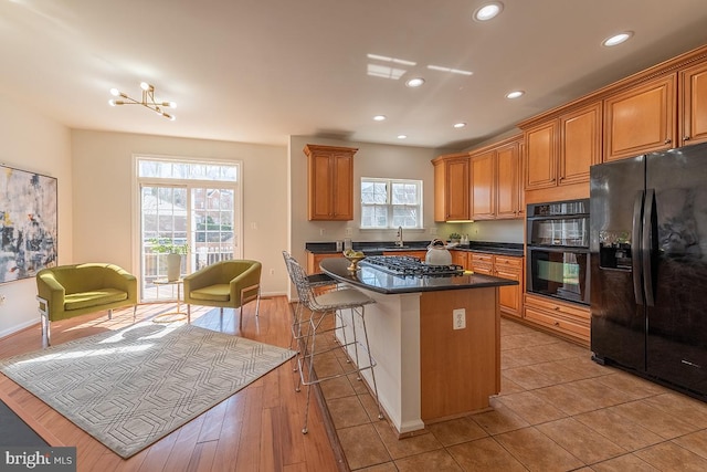 kitchen featuring recessed lighting, brown cabinets, black appliances, and a breakfast bar area