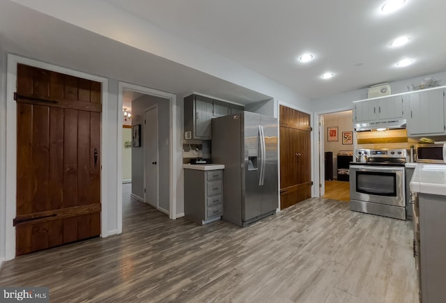 kitchen featuring light wood-style flooring, gray cabinetry, light countertops, under cabinet range hood, and appliances with stainless steel finishes