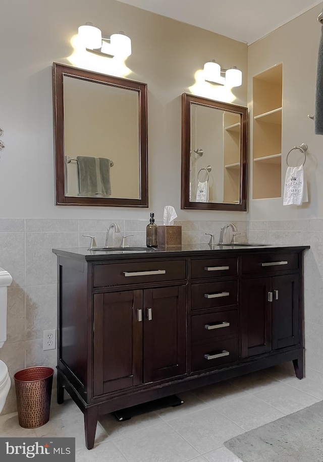 bathroom featuring tile patterned floors, toilet, a sink, tile walls, and double vanity