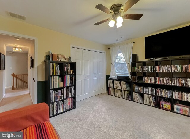 living area with an upstairs landing, visible vents, carpet floors, and ceiling fan