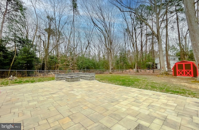 view of patio with an outdoor structure, a storage unit, fence, and an outdoor fire pit