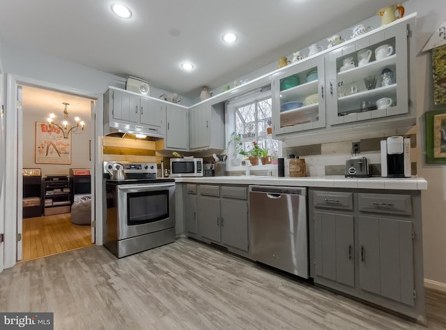 kitchen with light wood-style floors, gray cabinets, under cabinet range hood, and stainless steel appliances