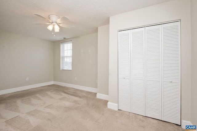 unfurnished bedroom featuring light carpet, a textured ceiling, a closet, and baseboards