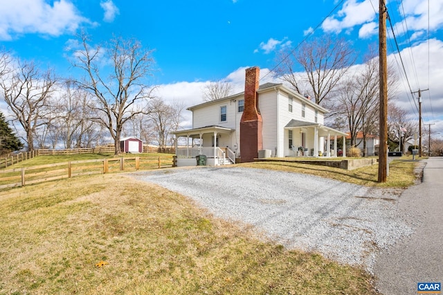 view of property exterior with driveway, a lawn, a chimney, covered porch, and fence