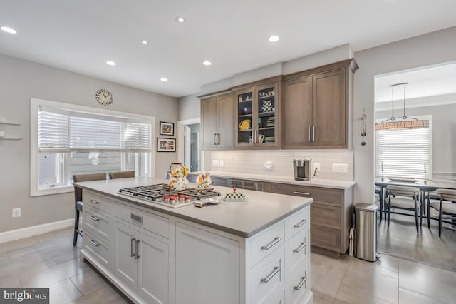 kitchen featuring tasteful backsplash, light countertops, stainless steel gas stovetop, glass insert cabinets, and a kitchen island