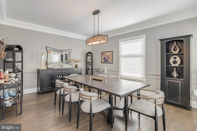 dining area with a wainscoted wall, a decorative wall, wood finished floors, and crown molding