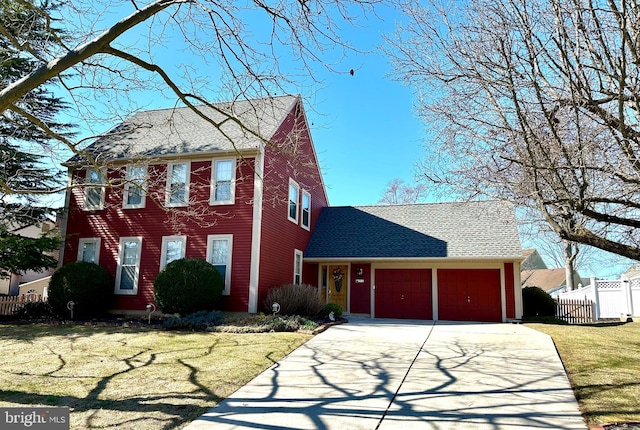 colonial house with a shingled roof, an attached garage, fence, driveway, and a front lawn