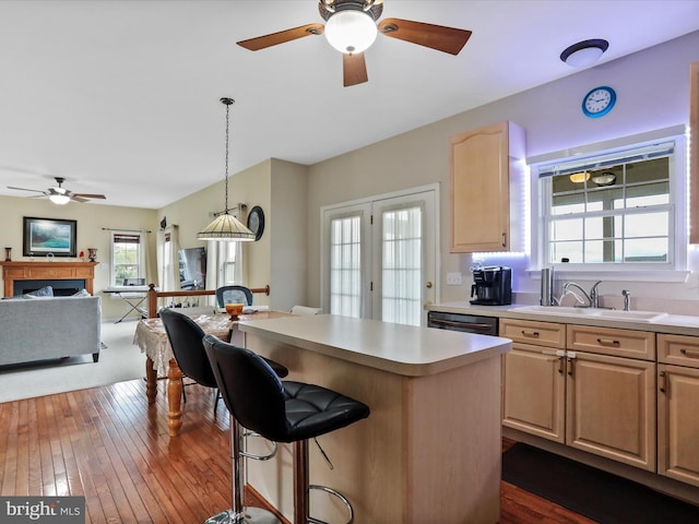 kitchen featuring light brown cabinetry, a breakfast bar, a fireplace, and dishwashing machine