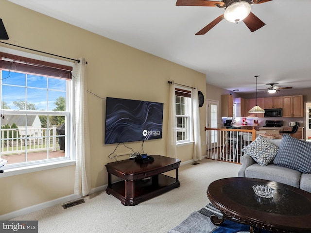 living area with light carpet, visible vents, baseboards, and ceiling fan