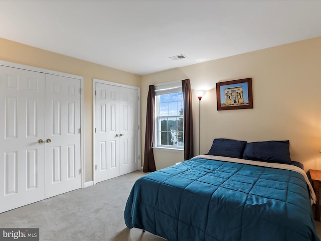 carpeted bedroom with two closets, visible vents, and baseboards