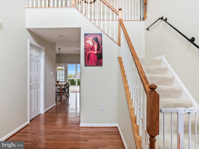 stairs with wood finished floors, a towering ceiling, and baseboards