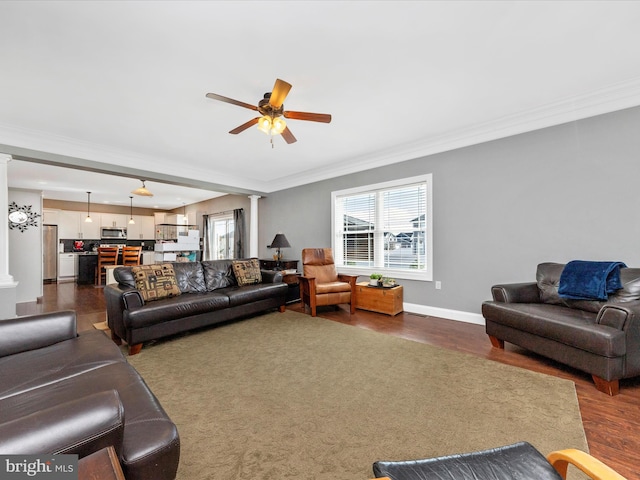 living room with dark wood-style floors, crown molding, baseboards, ceiling fan, and ornate columns