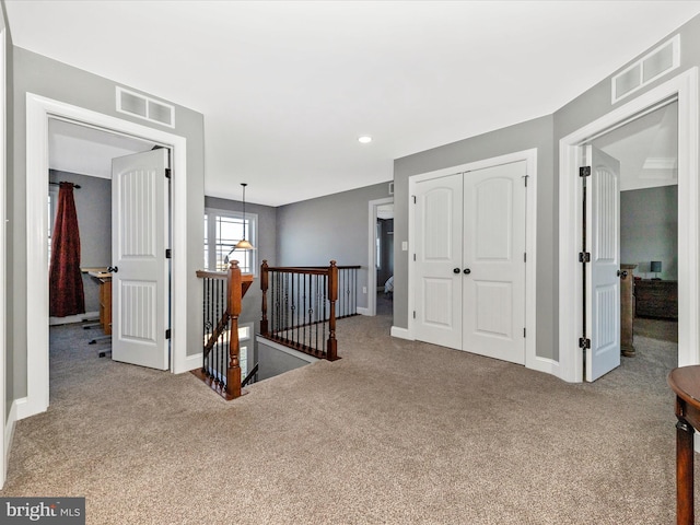 hall with an upstairs landing, visible vents, and carpet