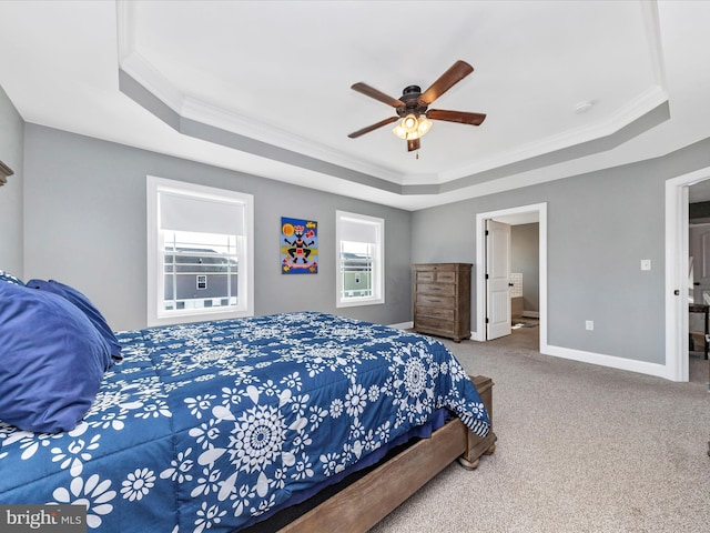 carpeted bedroom with a ceiling fan, a tray ceiling, connected bathroom, crown molding, and baseboards