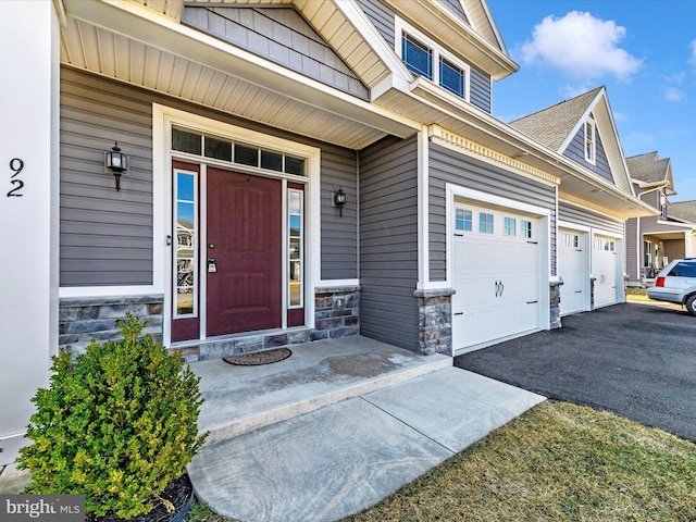 doorway to property featuring aphalt driveway, stone siding, and a garage