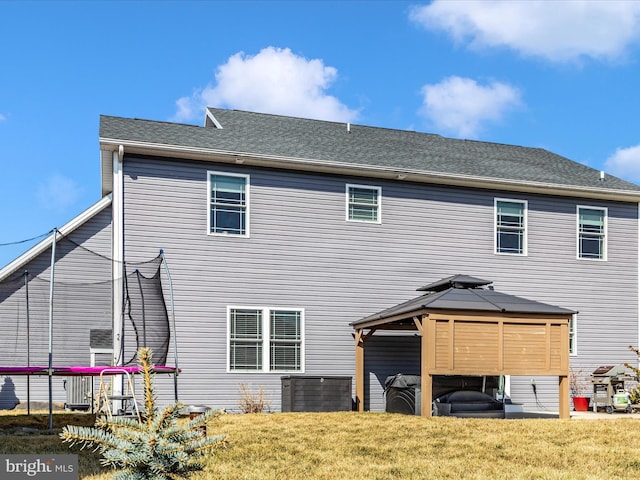 back of house featuring a gazebo, a yard, a trampoline, and roof with shingles