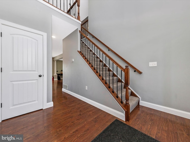 staircase with a towering ceiling, visible vents, baseboards, and wood finished floors