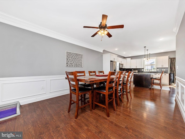 dining space featuring a wainscoted wall, dark wood-type flooring, ornamental molding, a ceiling fan, and recessed lighting