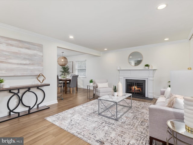 living area featuring baseboards, a glass covered fireplace, ornamental molding, wood finished floors, and recessed lighting