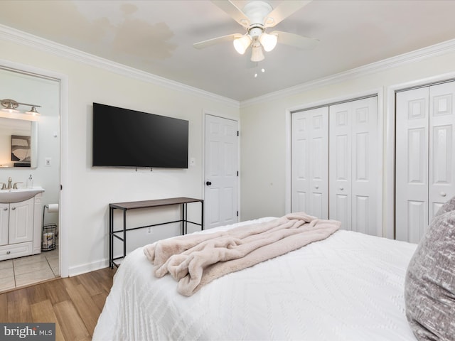 bedroom featuring baseboards, ceiling fan, crown molding, light wood-style floors, and multiple closets