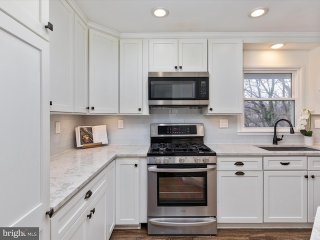 kitchen featuring light stone counters, stainless steel appliances, tasteful backsplash, white cabinetry, and a sink