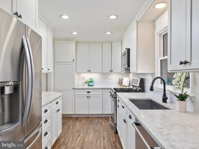 kitchen featuring wood finished floors, a sink, white cabinetry, appliances with stainless steel finishes, and tasteful backsplash