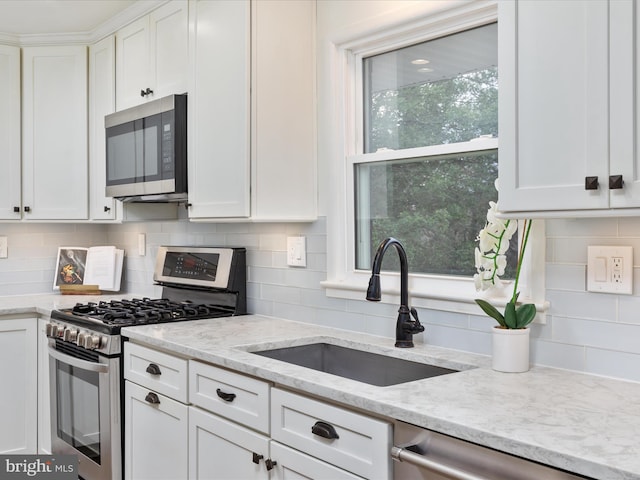 kitchen with white cabinets, light stone counters, appliances with stainless steel finishes, a sink, and backsplash