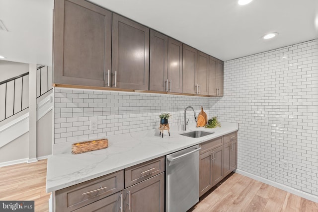 kitchen with light stone counters, backsplash, stainless steel dishwasher, light wood-style floors, and a sink