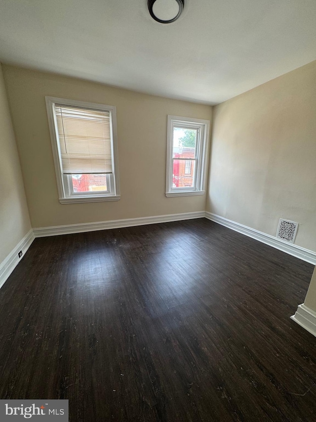 spare room with dark wood-style floors, visible vents, and baseboards