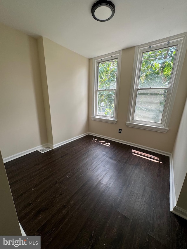 unfurnished room with dark wood-style floors, visible vents, and baseboards