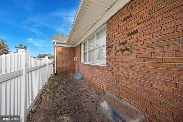 view of side of property with fence, brick siding, and a shingled roof