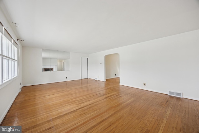 unfurnished living room with arched walkways, visible vents, light wood finished floors, and baseboards