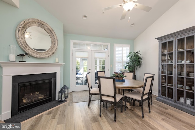 dining room with a fireplace with flush hearth, wood finished floors, a ceiling fan, vaulted ceiling, and french doors