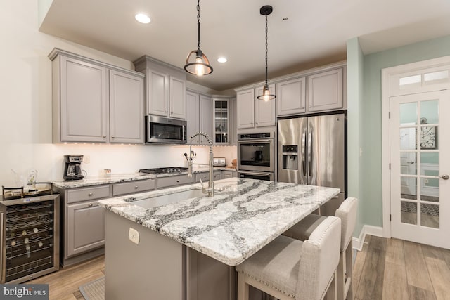 kitchen featuring gray cabinetry, beverage cooler, stainless steel appliances, light wood finished floors, and glass insert cabinets