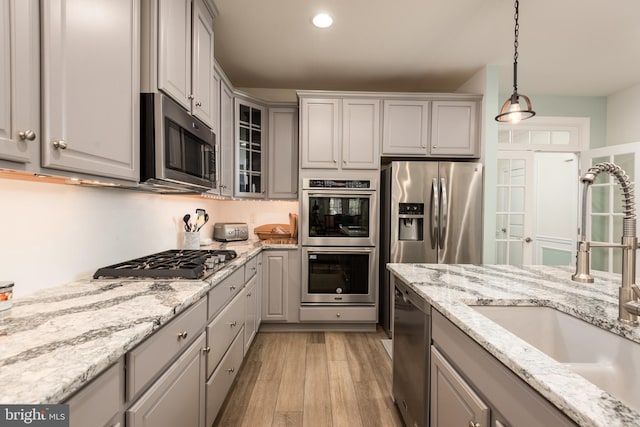 kitchen featuring light wood finished floors, gray cabinetry, appliances with stainless steel finishes, glass insert cabinets, and a sink