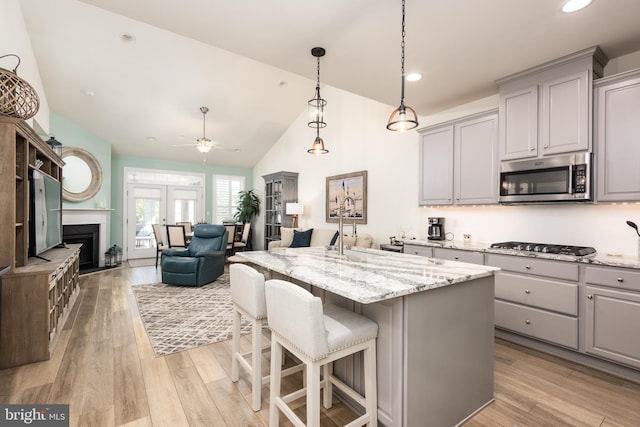 kitchen with light wood finished floors, appliances with stainless steel finishes, light stone countertops, and gray cabinetry